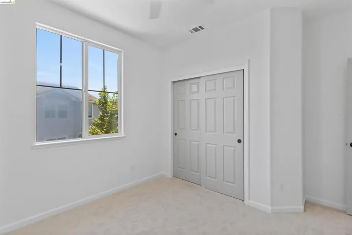 Light-filled room featuring a large window, neutral carpeting, white baseboards, and a bi-fold closet with panel doors