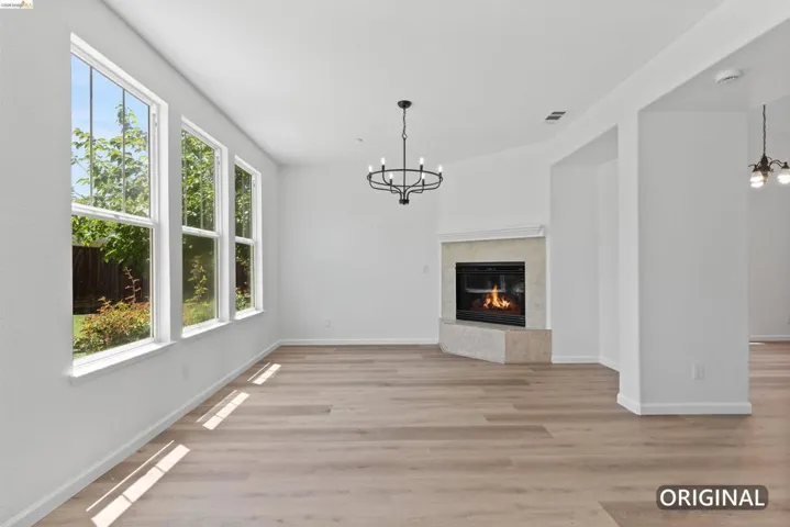 Living area featuring wood-finish flooring, a corner fireplace with stone surround, a mantel, three large windows, and an overhead chandelier