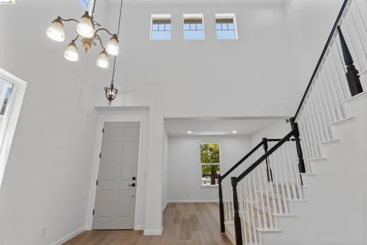 Two-story foyer featuring a staircase with black newel posts and white spindles, wood-finish flooring, high ceilings, and an overhead chandelier