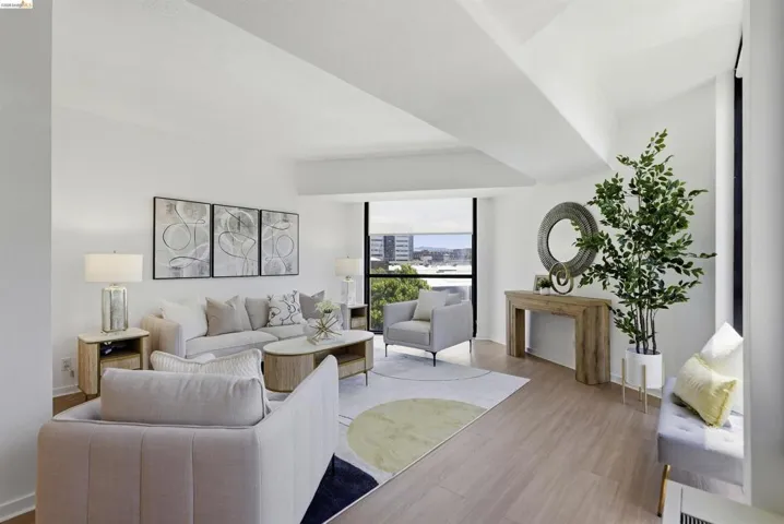 Spacious living area featuring large windows, light wood-finish flooring, and white walls