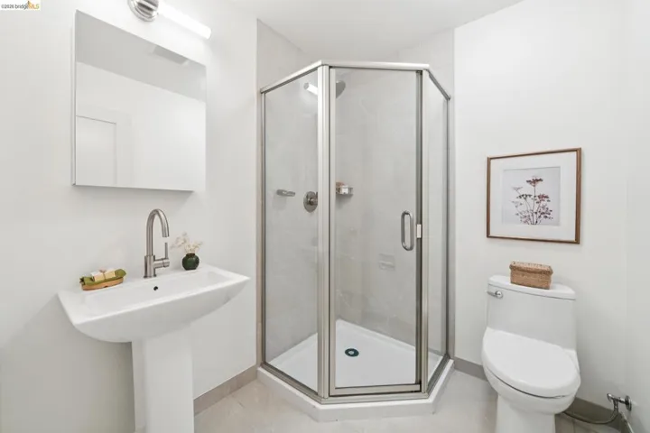 Bathroom featuring a corner glass-enclosed shower, pedestal sink with a brushed nickel faucet, wall-mounted mirror, and tile flooring