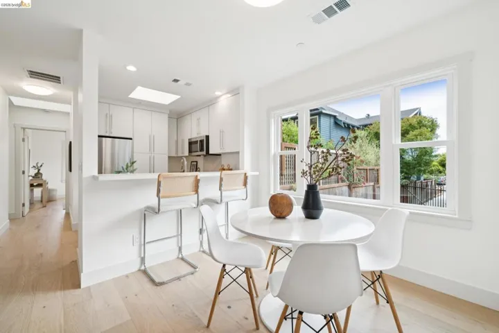 Open-concept kitchen with light wood-finish flooring, white cabinetry, stainless steel appliances, and a breakfast bar