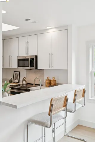 Kitchen featuring a white countertop with breakfast bar seating, a stainless steel microwave, a built-in cooktop, and light wood-finish flooring