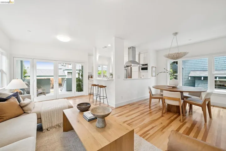 Open-concept living area featuring wood-finish flooring, a wall of glass patio doors, built-in kitchen peninsula with bar seating, a stainless steel range hood, and multiple windows