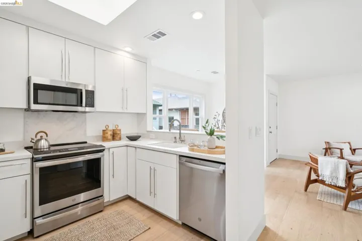 Kitchen featuring stainless steel appliances, white cabinetry, a skylight, light-toned wood-finish flooring, and a window with exterior views