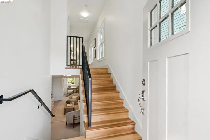 Entry foyer with wood-finish stairs, white paneled door with transom window, and contemporary black metal railings