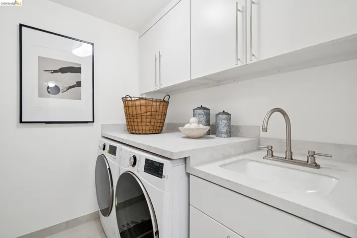 Laundry area featuring white cabinetry, built-in sink with a brushed nickel faucet, light-toned countertop, and tile flooring