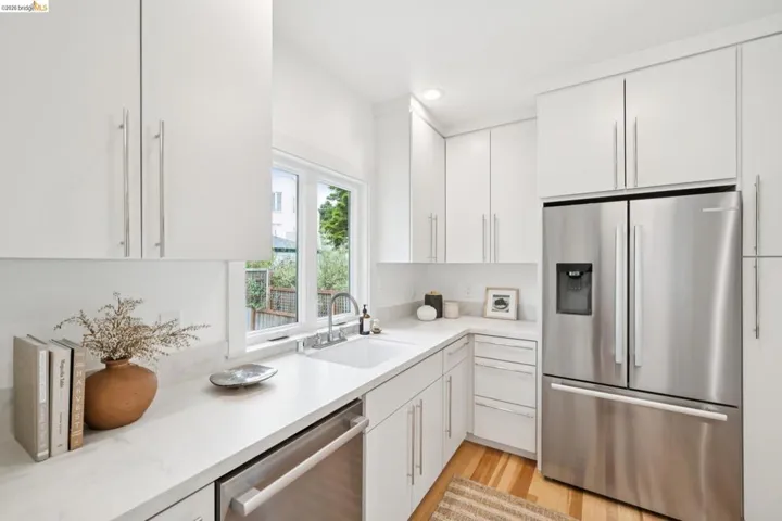 Modern kitchen featuring white cabinetry, light-toned countertops, stainless steel appliances, a stainless steel sink with a chrome faucet, and wood-finish flooring