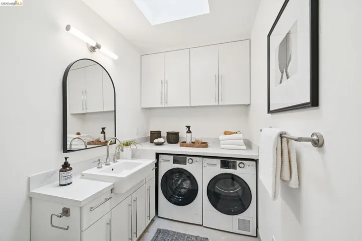White laundry room featuring a skylight, white cabinetry, a built-in sink, and integrated appliances