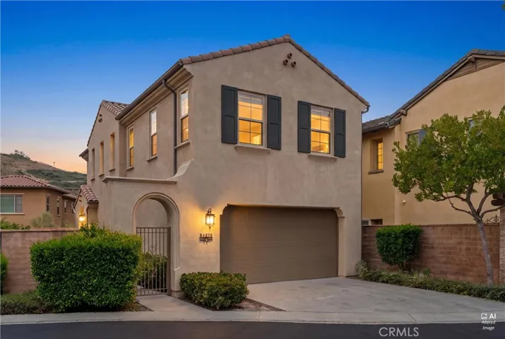 Front elevation featuring a gated entry courtyard, attached two car garage, stucco exterior, decorative shutters, and exterior lighting.