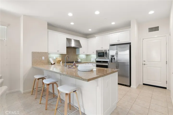 Kitchen featuring shaker style cabinetry, stainless steel appliances, granite countertops, breakfast bar seating, and recessed lighting.
