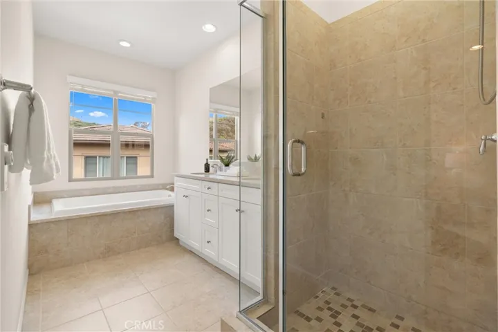 Primary bathroom featuring dual vanities, a soaking tub, separate glass enclosed shower, and abundant natural light.