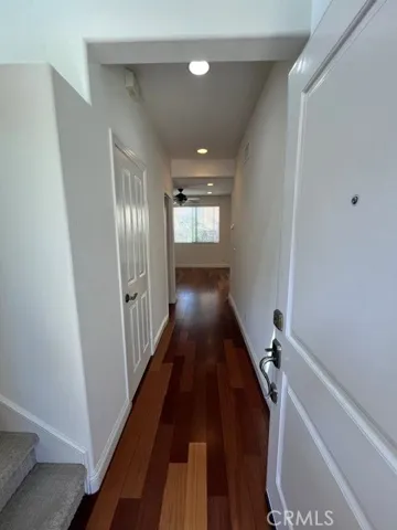 A bright and inviting hallway showcases rich hardwood flooring, crisp white walls, and elegant wainscoting that adds architectural character. Recessed lighting enhances the clean, modern aesthetic, while natural light from the window at the end of the corridor creates an open and airy feel. Multiple doorways provide convenient access to adjacent rooms, and the well-maintained finishes contribute to the home's polished appearance.