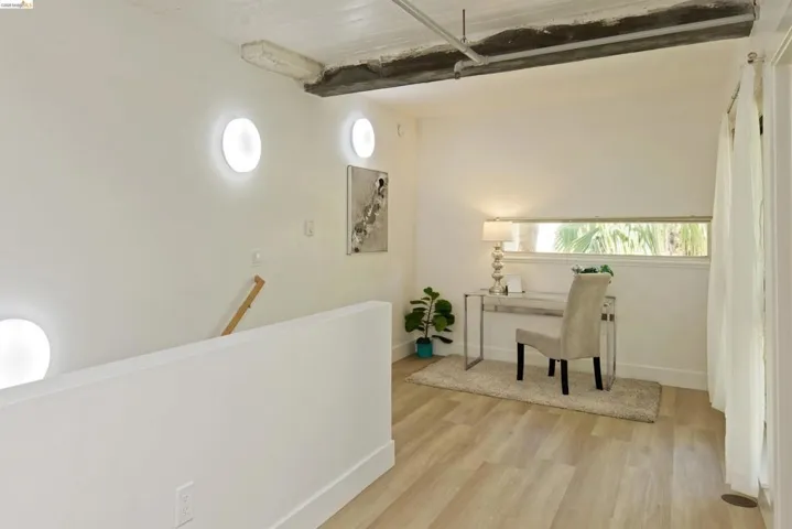 Corridor featuring light wood finished floors, beam ceiling, and an upstairs landing