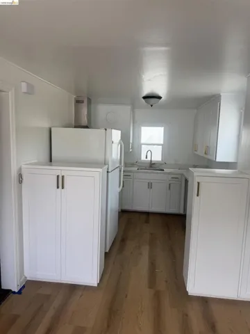 Bright kitchen featuring extensive white cabinetry, wood-finish flooring, a stainless steel range hood, and a window above the sink