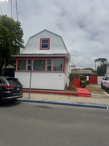 White exterior with a prominent red trim, featuring a gambrel roof and decorative shingle siding on the upper level