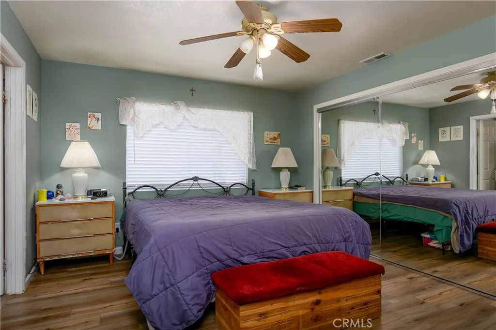 The generous primary bedroom suite provides a relaxing retreat. The space highlights continuous wood-look flooring, soft sage-green walls, and expansive floor-to-ceiling mirrored closet doors that amplify the natural light filtering through the large window.