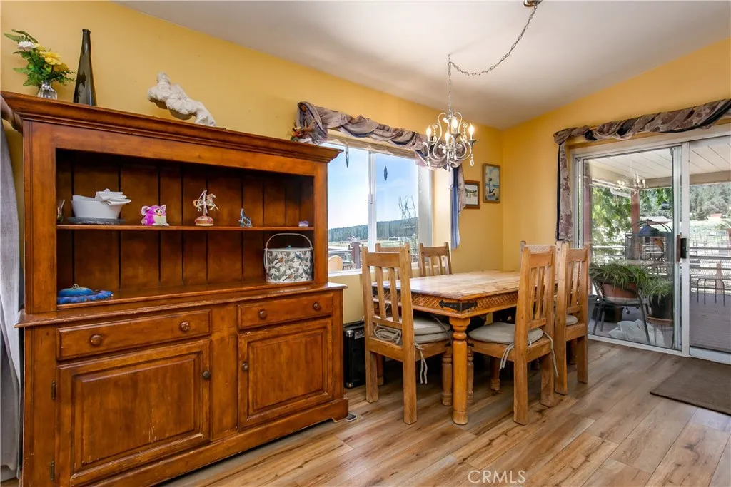 The warm and inviting dining space showcases an open layout with beautiful wood-look flooring and soft yellow-toned walls. It features a rustic wooden dining table set and a matching large wooden display hutch, while a wide sliding glass door fills the room with natural light and provides direct access to the outdoor deck.