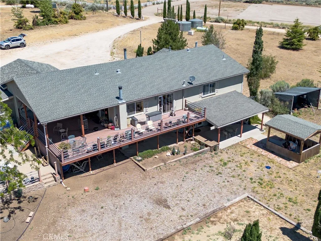A detailed aerial perspective highlighting the rear of the residence, showcasing the expansive multi-level wooden deck perfect for entertaining, a detached covered patio gazebo, and a broad view of the driveway and surrounding property.