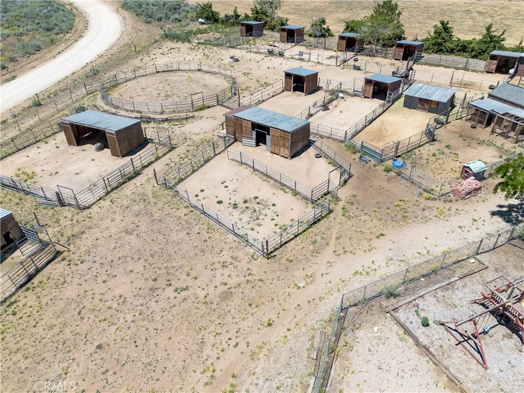 An elevated aerial perspective highlighting the property's equestrian setup, featuring multiple horse stalls, covered shelters, fenced corrals, and open paddocks.