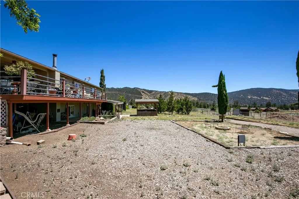 Ground-level view of the home's side profile, featuring an upper-level balcony deck, wide open side yard, and a beautiful mountain backdrop.