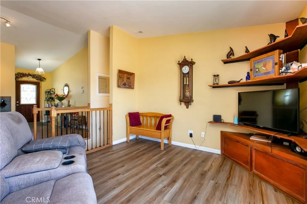 The welcoming living room boasts an open feel with impressive vaulted ceilings and beautiful wood-look flooring. Warm-toned walls complement a large built-in media center and shelving unit, while a decorative wooden railing opens up to the neighboring dining area and entryway.