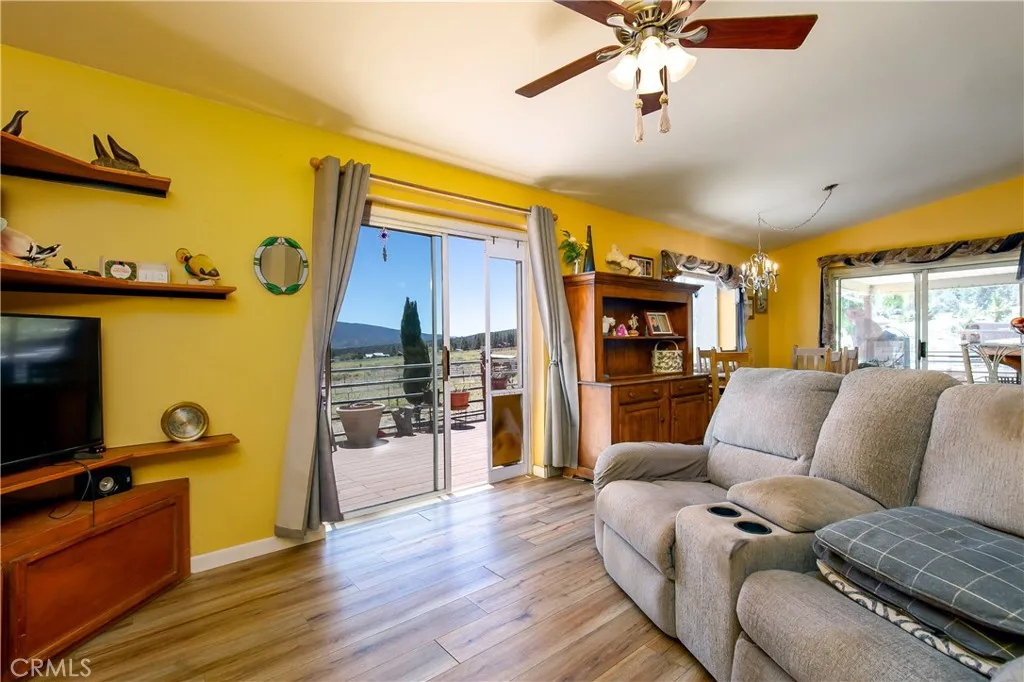 An open-concept living space showcasing a cozy seating arrangement and rich wood-look flooring. A vibrant warm accent wall complements the light-filled layout, while massive sliding glass doors frame scenic property views and provide effortless access to the expansive outdoor viewing deck.