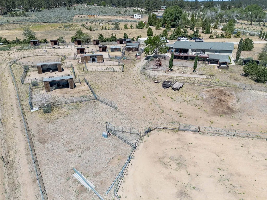 An expansive aerial view highlighting a large, fenced equestrian riding arena alongside stable facilities, shelters, and open pastures, all set against a beautiful mountain backdrop.