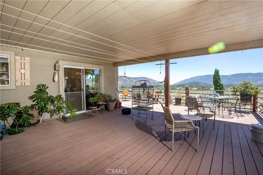 An impressive outdoor living space perfect for entertaining. This large, covered wooden deck features a spacious layout with room for multiple seating arrangements, a dining area, and potted plants, all framed by a sturdy railing overlooking stunning, panoramic mountain and valley views.