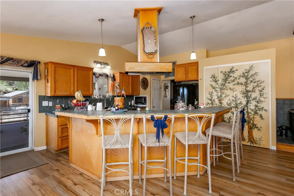 An expansive, open-concept view highlighting the home's main entertaining hub. The spacious kitchen features a large wrap-around breakfast bar island with comfortable counter seating, extensive warm oak cabinetry, and unique overhead lighting, flowing seamlessly into a bright dining area perfect for gatherings.