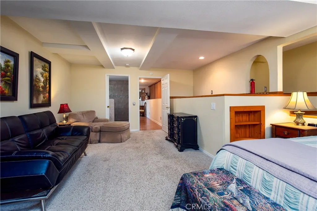 A spacious secondary angle of the 5th lower-level bedroom suite. This wide perspective showcases the room's extensive square footage, bright recessed ceiling lights, and neutral carpeting, while illustrating how the room opens up to a relaxed sitting lounge area perfect for a multi-generational living setup.