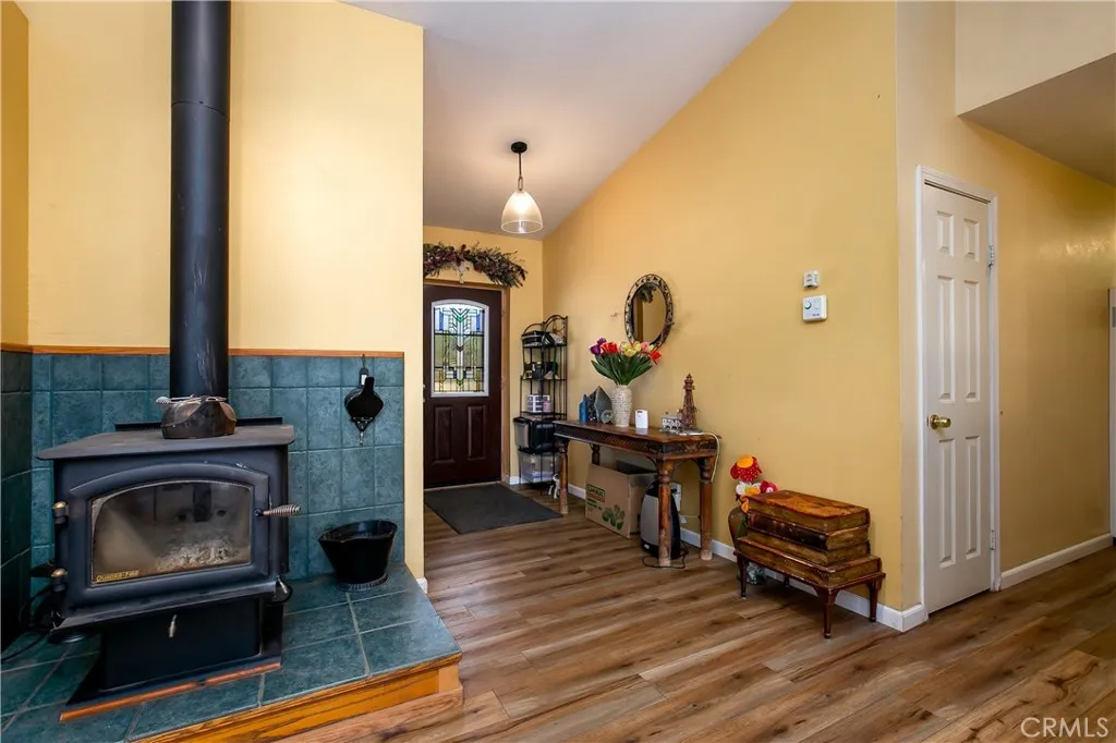 A warm and inviting look at the home's main living entry. This shot highlights the durable wood-look flooring, neutral earth-toned walls, and an elegant wood-burning stove on a custom tiled hearth. The view flows past a charming decorative alcove toward the front door entry.