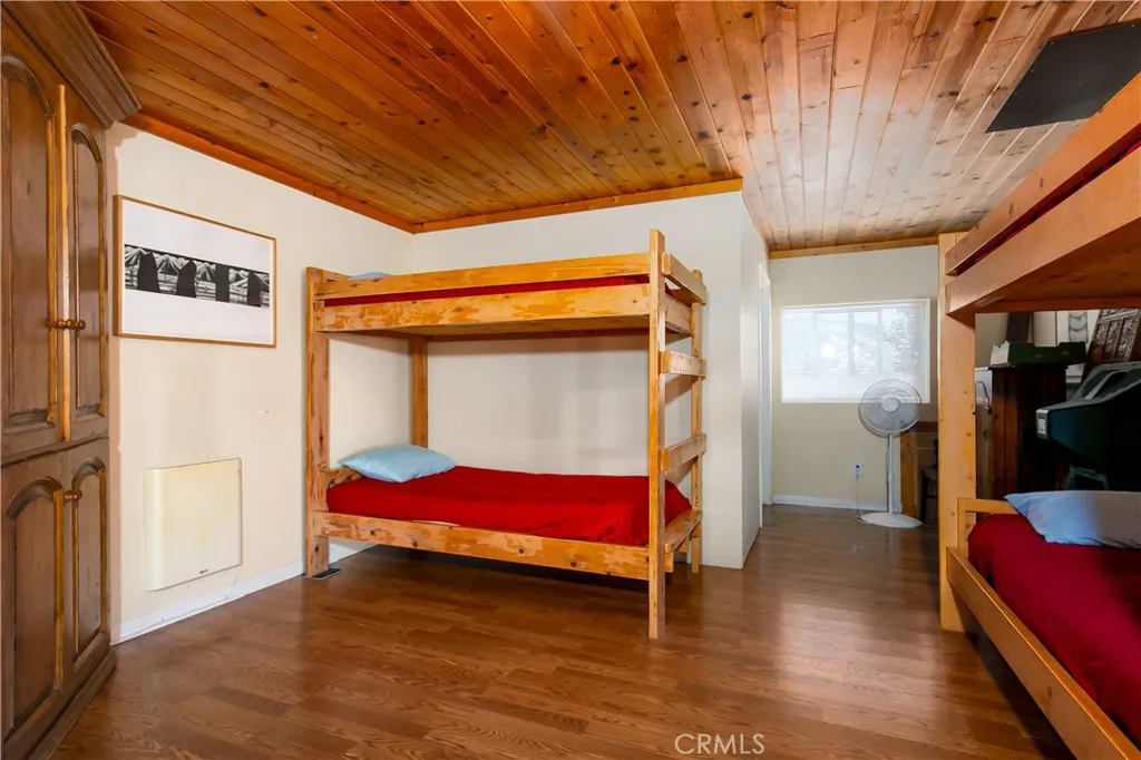 Spacious bonus room or flexible living area in the private downstairs suite, featuring cream-colored walls with crisp white trim, rich wood flooring, and a warm natural wood-paneled ceiling.