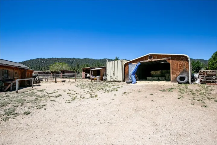 A functional ground-level shot showcasing a spacious, rustic wooden outbuilding with a wide open-front entry. Perfect for storing ranch equipment, feed, or tools, this structure sits alongside fenced corral areas with a scenic mountain backdrop.
