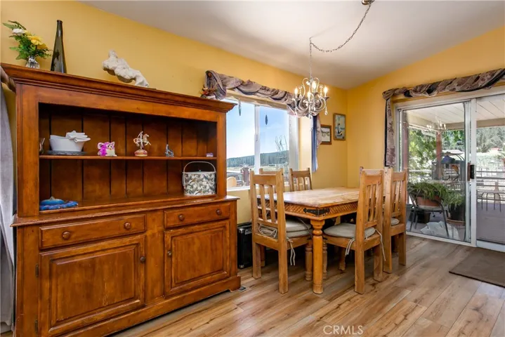 The warm and inviting dining space showcases an open layout with beautiful wood-look flooring and soft yellow-toned walls. It features a rustic wooden dining table set and a matching large wooden display hutch, while a wide sliding glass door fills the room with natural light and provides direct access to the outdoor deck.