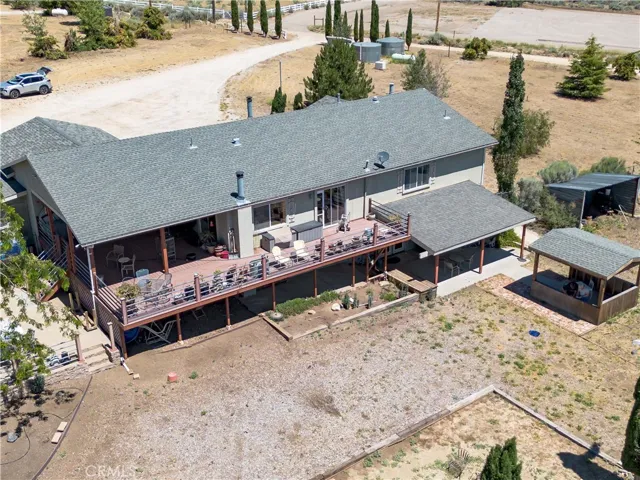 A detailed aerial perspective highlighting the rear of the residence, showcasing the expansive multi-level wooden deck perfect for entertaining, a detached covered patio gazebo, and a broad view of the driveway and surrounding property.