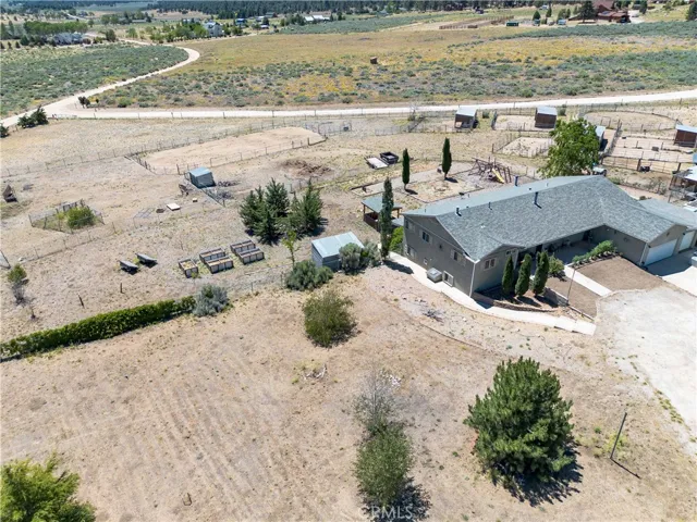 A high-angle aerial view looking from the northwest, showcasing the main residence, its spacious layout, and the adjacent property grounds including mature trees, pathways, and the expansive landscape beyond.
