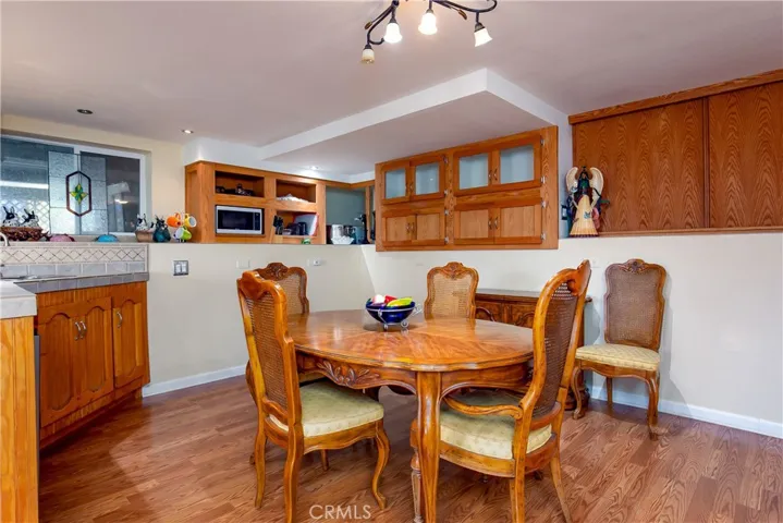 Another perspective of the downstairs dining space within the private suite. This view showcases the continuous rich wood flooring, warm wood upper cabinets, track lighting, and a traditional wooden dining table set, demonstrating a comfortable and inviting atmosphere for meals and gatherings.