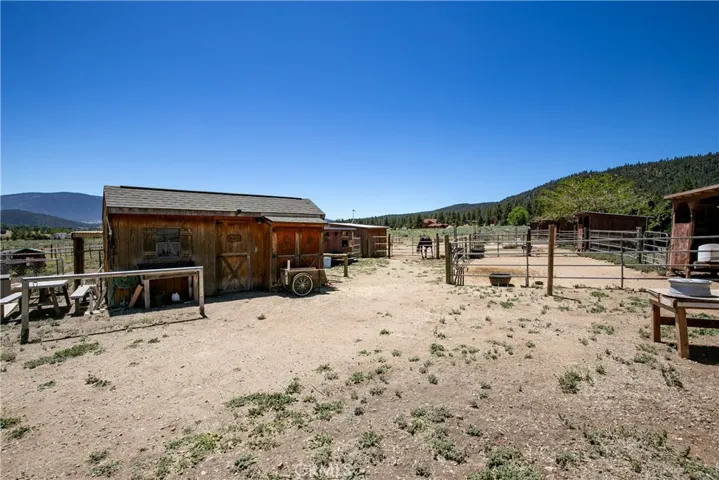 A functional ground-level perspective highlighting the property's outdoor equestrian infrastructure. This shot captures the secure cross-fenced corrals, open horse pens, and outdoor staging areas, all framed by a scenic mountain and tree-lined landscape.