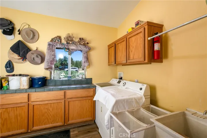 The home's dedicated laundry and utility space. This practical room features oak upper and lower cabinetry, a built-in utility sink with counter space, laundry hookups, and soft yellow-toned walls complete with a convenient wall-mounted coat and hat rack.
