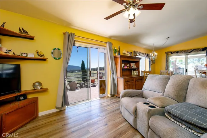 An open-concept living space showcasing a cozy seating arrangement and rich wood-look flooring. A vibrant warm accent wall complements the light-filled layout, while massive sliding glass doors frame scenic property views and provide effortless access to the expansive outdoor viewing deck.