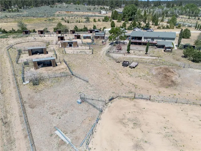 An expansive aerial view highlighting a large, fenced equestrian riding arena alongside stable facilities, shelters, and open pastures, all set against a beautiful mountain backdrop.