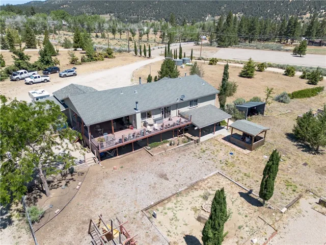 An elevated aerial perspective showcasing the main home's expansive deck, detached structures, and the scenic, tree-lined property with mountain views in the background.