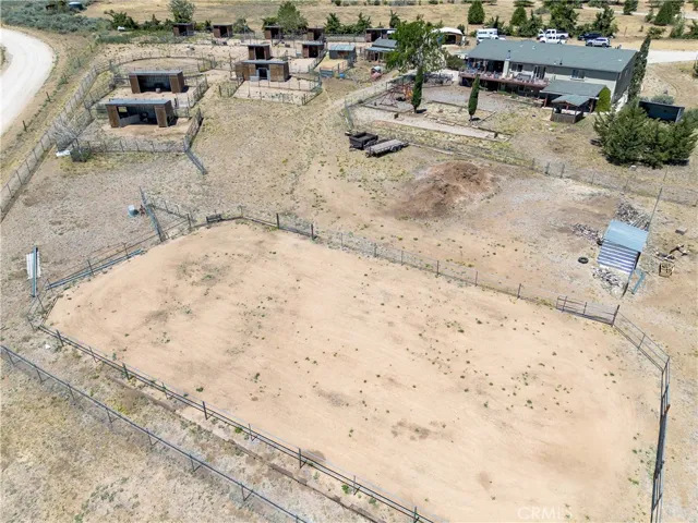 An expansive, elevated aerial perspective that showcases the extensive footprint of the property, highlighting the massive fenced riding arena, covered horse stalls, and the main residence with its expansive deck.