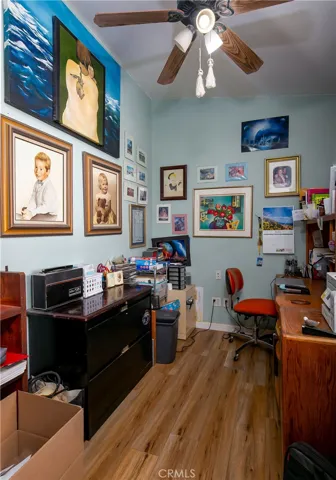 A versatile home office or creative studio space. This practical room features a large wooden desk with ample storage cabinetry, light blue walls, a classic wood-paddle ceiling fan, and durable flooring, offering a perfect private work-from-home setup.