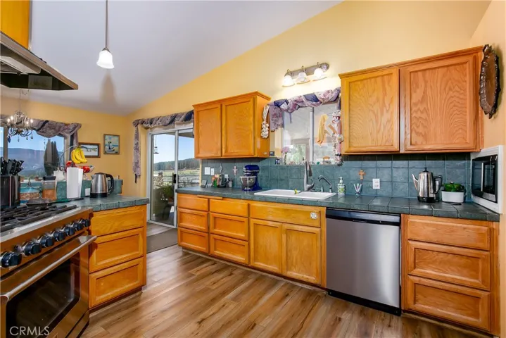 A secondary view of the kitchen highlighting the functional workspace. This perspective features an under-mount sink, a stainless steel dishwasher, a classic teal-tiled backsplash, and abundant warm wood cabinet storage, all adjacent to sliding glass doors that open to the outdoor deck area.