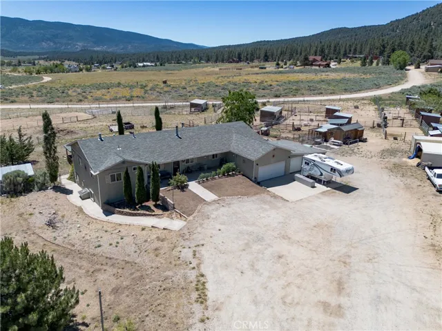 A higher aerial perspective capturing the side and rear profile of the home, highlighting the transition from the residential driveway to the open pastures, equestrian areas, and scenic mountain range in the distance.