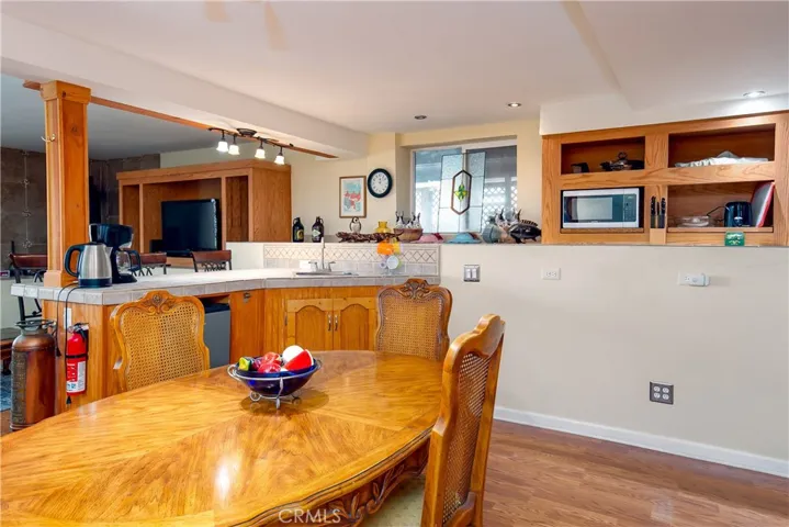 A view of the functional kitchen and dining space located inside the private downstairs suite. This area features continuous wood flooring, a cozy dining setup, a raised breakfast bar counter, and warm oak upper and lower cabinetry with integrated appliances, perfect for independent guest living or rental potential.
