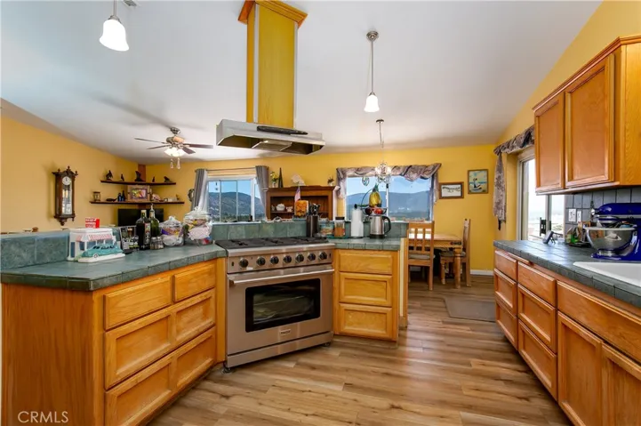 A comprehensive view of the kitchen highlighting the high-end THOR 6-burner propane range and overhead ventilation. This shot beautifully captures the expansive wrap-around counters, rich wood-look flooring, and ample cabinetry, flowing seamlessly toward a bright dining nook and outdoor deck access.