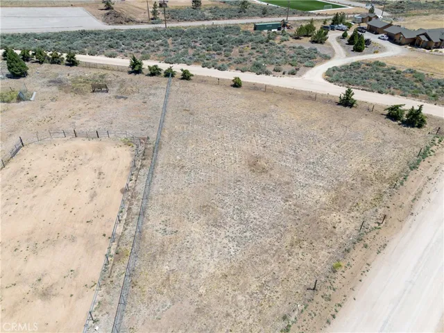 Broad, high aerial perspective showcasing the property's vast acreage and open fields, with a clear view of the equestrian enclosures, winding driveway, and main home nestled in the distance.